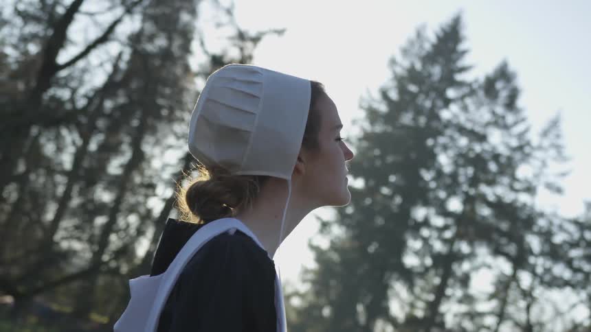 A pilgrim stands in a forest on a sunny day