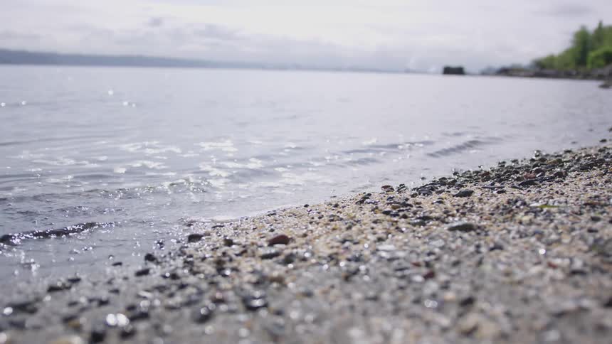 The waves of an ocean flow toward a shore of pebbles
