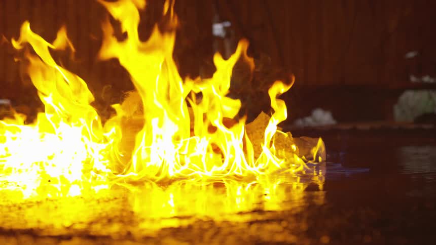 A doll being caught on fire and dropped into an gas on the ground creating a larger fire
