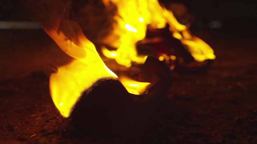 A large piece of wood burns in a fire separate from a pile of wood that is also on fire