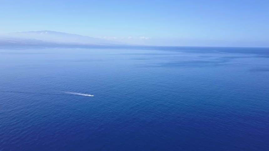 Boat sails on clear blue ocean with mountains in background