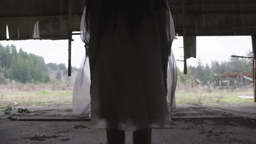 A woman's dress rustling in the wind as she stands in a ruined building
