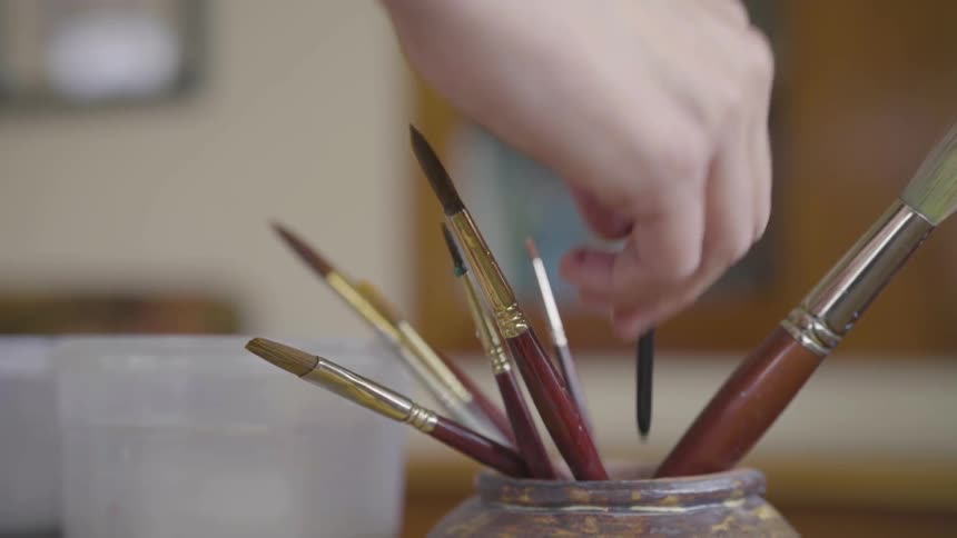 A person washing his paint brushes in a bucket of water
