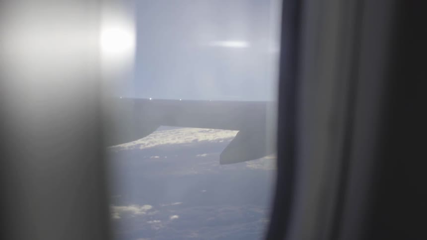 An airplane wing is being viewed from a seat inside the airplane as it flies
