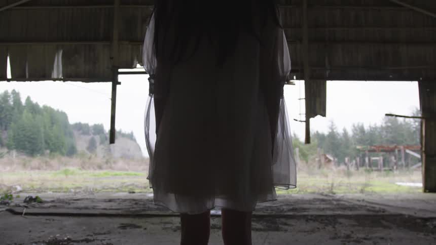 A girl in a white dress stands in an abandoned building