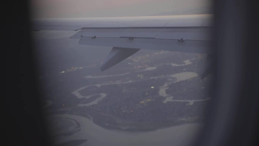 An airplane wing and the terrain below seen through a passenger window