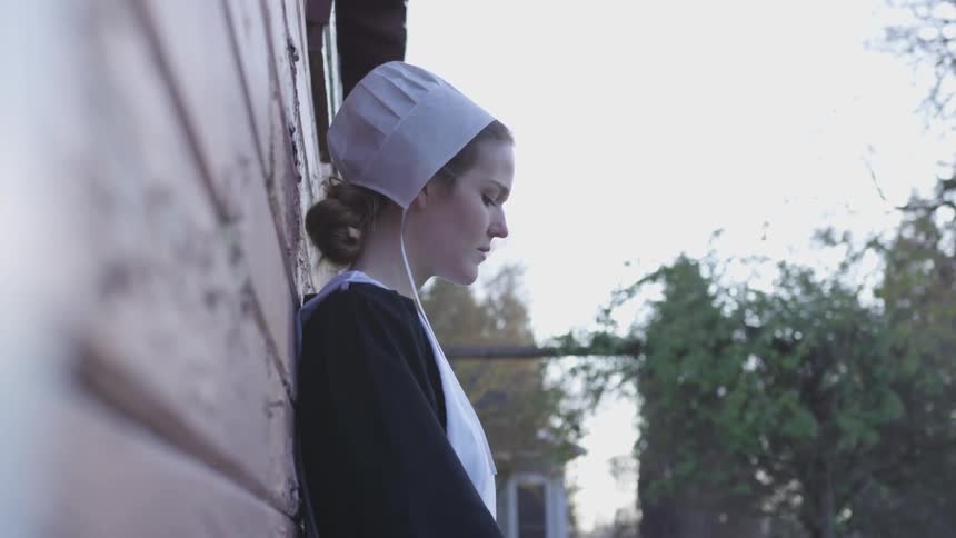 A woman leaning against a barn in deep thinking