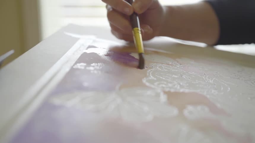 A person's right hand painting on a canvas indoors