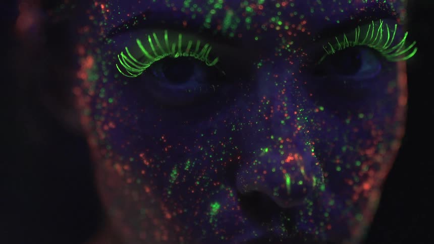 Woman with neon glow in the dark paint stares in a dark room