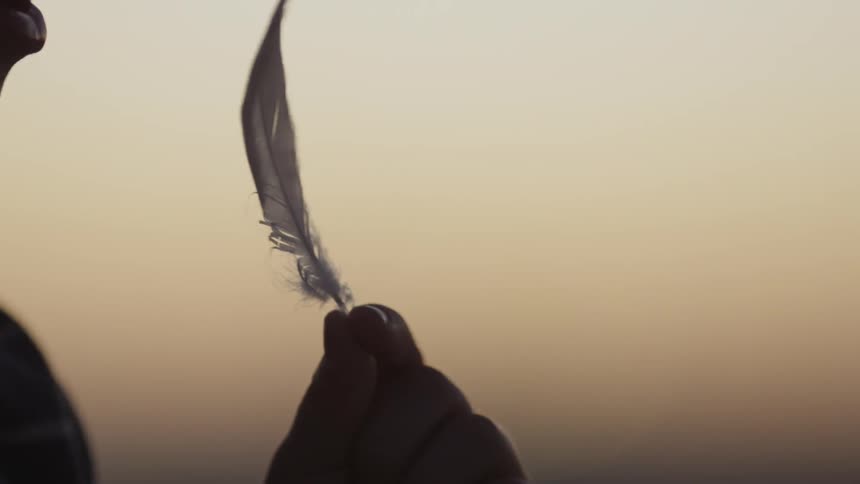 A person stands outside holding a feather and blows on it
