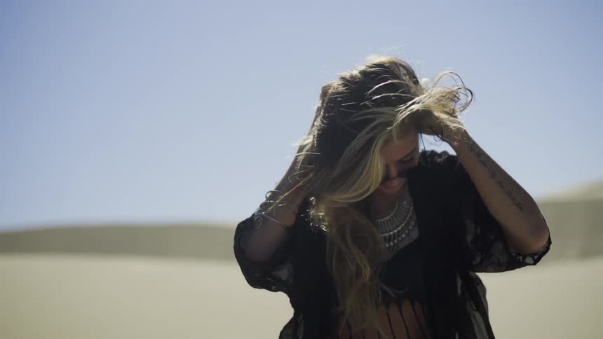 A woman with long, blonde hair playing with her hair, smiling and turning to walk away