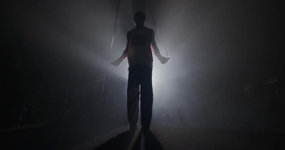 Man jumping rope in a dark room with one light
