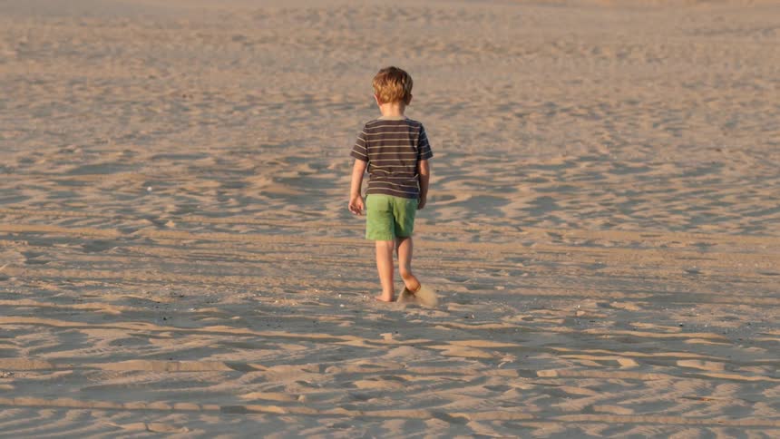 A little boy walks in the sand of a beach