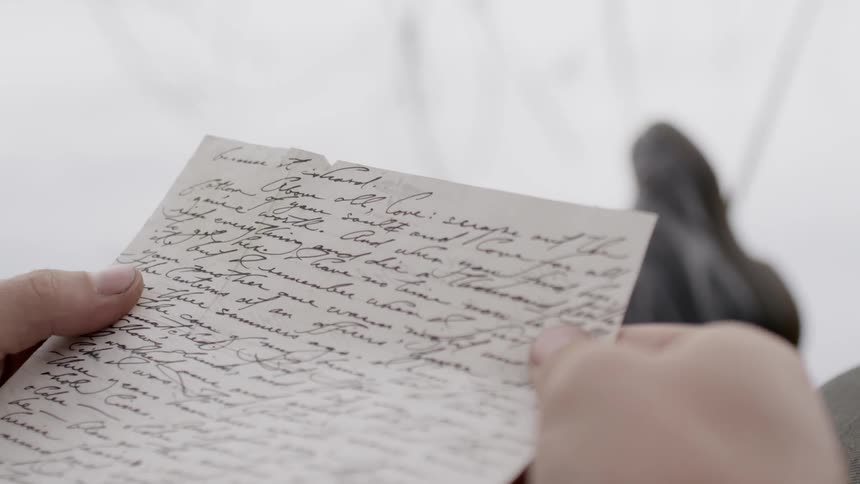 A man reads a handwritten letter outdoors on an overcast day