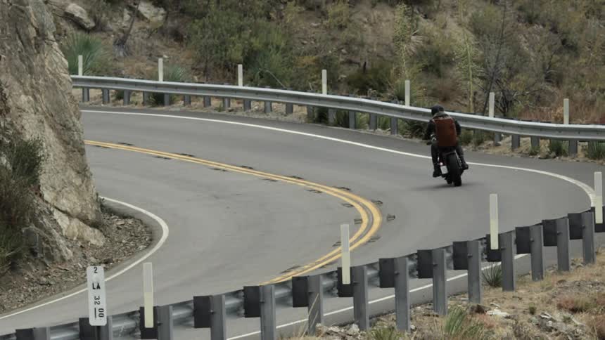 Man riding a motorcycle turns on a cliffside road