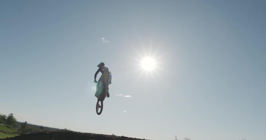 A dirt bike flies overhead during a jump on a dirt track