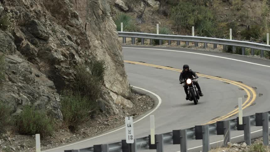A man on a motorcycle rides around the bend of a mountain road