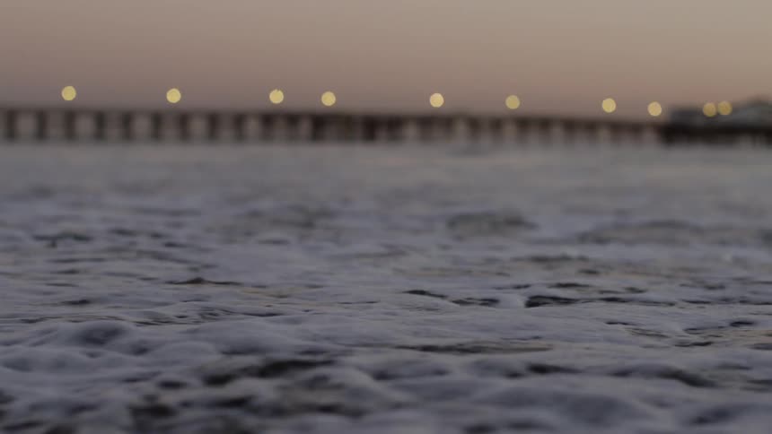 Ocean waves rolling into the beach with a bridge in the background