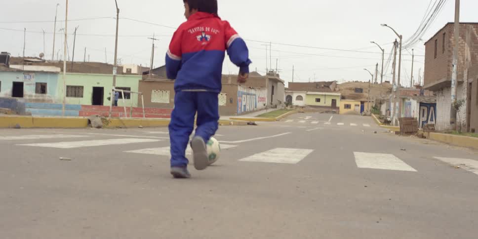 A boy kicks a soccer ball down the street