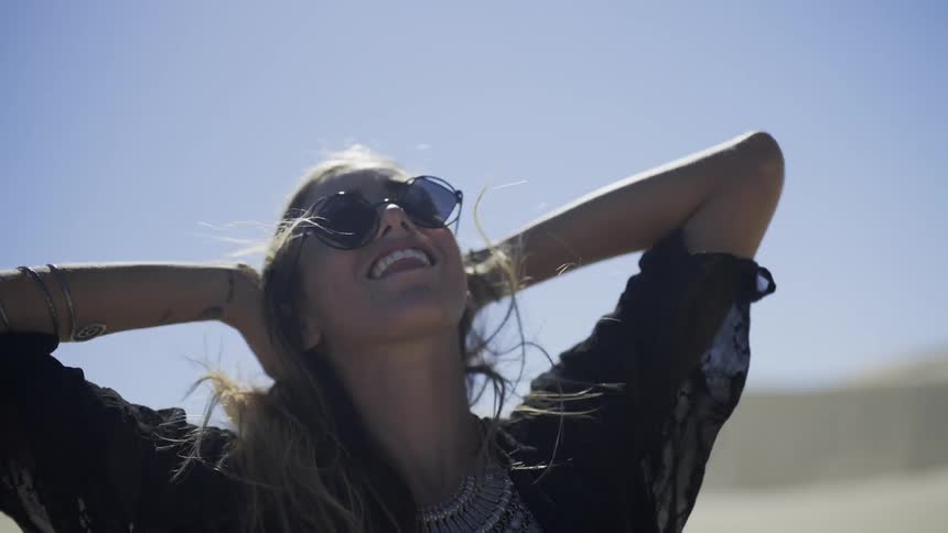 A woman pulls back her hair and lifts her smiling face to the sun