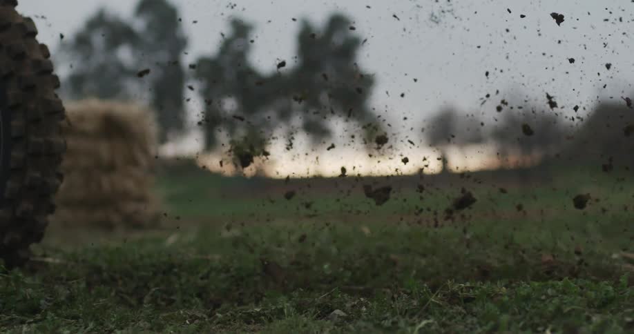 A dirt bike's rear tire kicks up dirt and grass as it moves