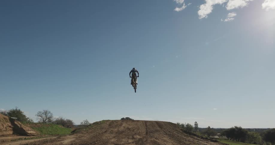 A man on a dirt bike flies overhead during a jump on a dirt track
