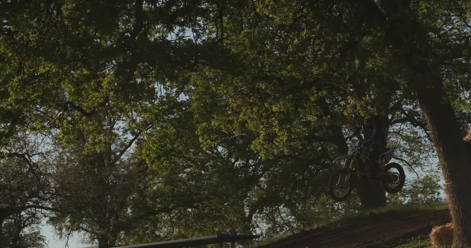 A man flies through the air on a motorcycle as it speeds down a grassy hill