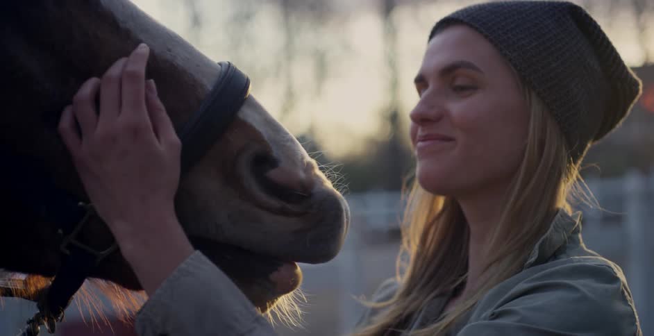 Woman pets a horse as the sun rises behind