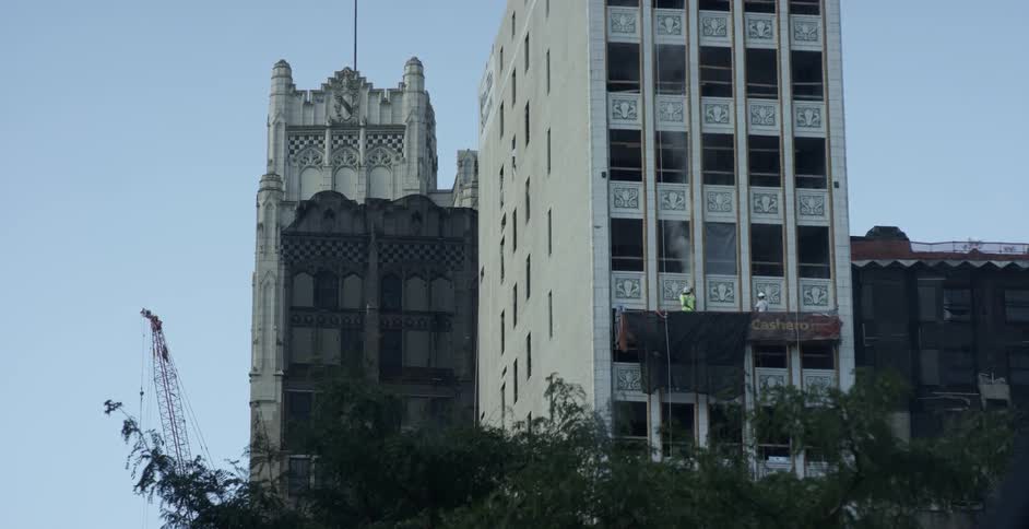 A crane is visible behind buildings under repair against a blue sky