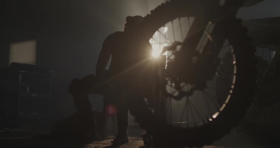 Man is lacing up boots with a motorcycle wheel blocking him