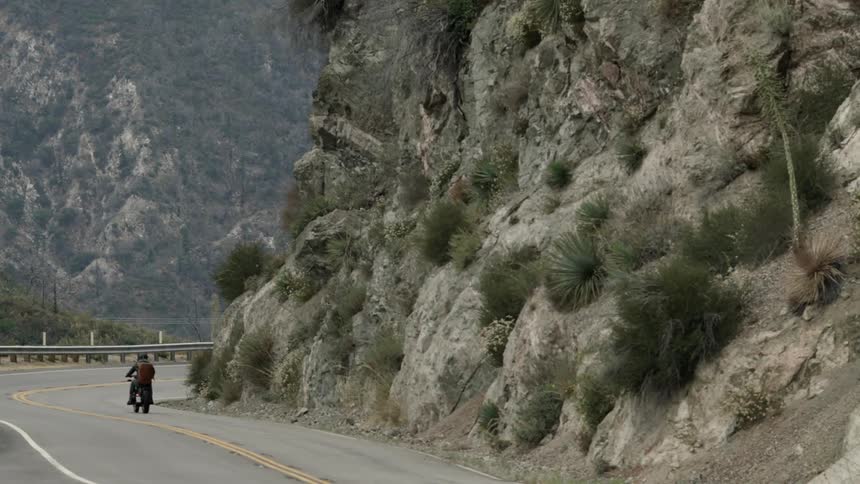 Person rides a motorcycle on a highway surrounded by mountains