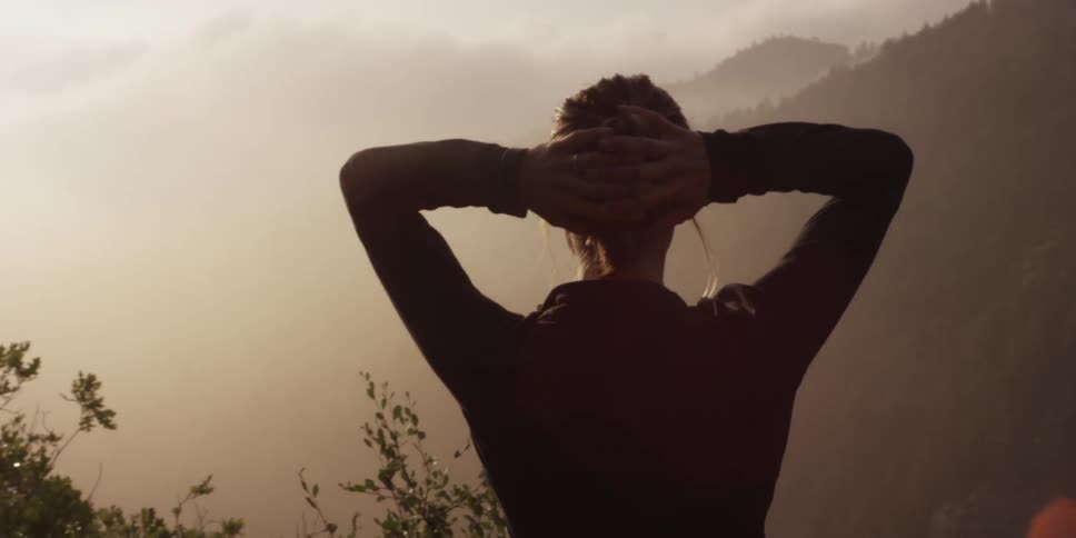 Woman views a foggy mountain range with her hands behind her head
