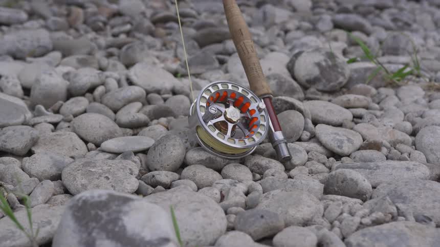 A fishing rod and its reel and fishing line is seen sitting on rock covered ground