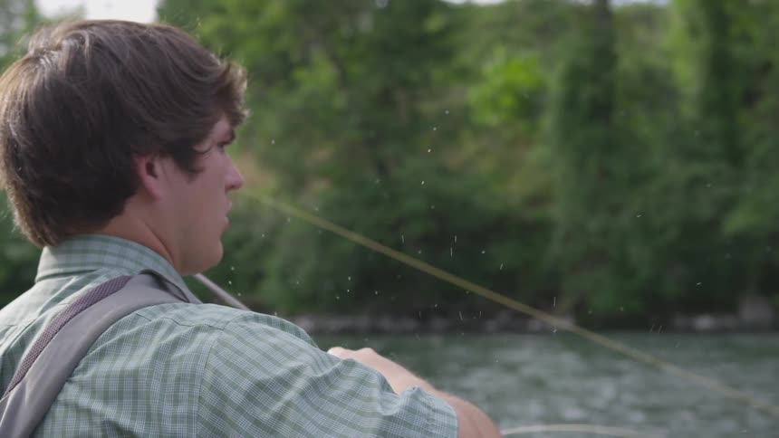 A man flicks a fly fishing pole as he casts into a river