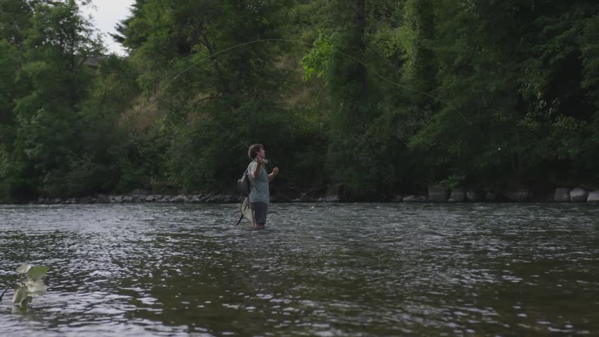 A man standing in a river casting a fishing line in the forest