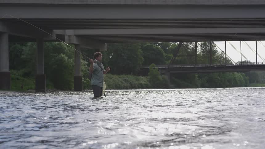Man fishing in the stream under the bridge on a sunny day
