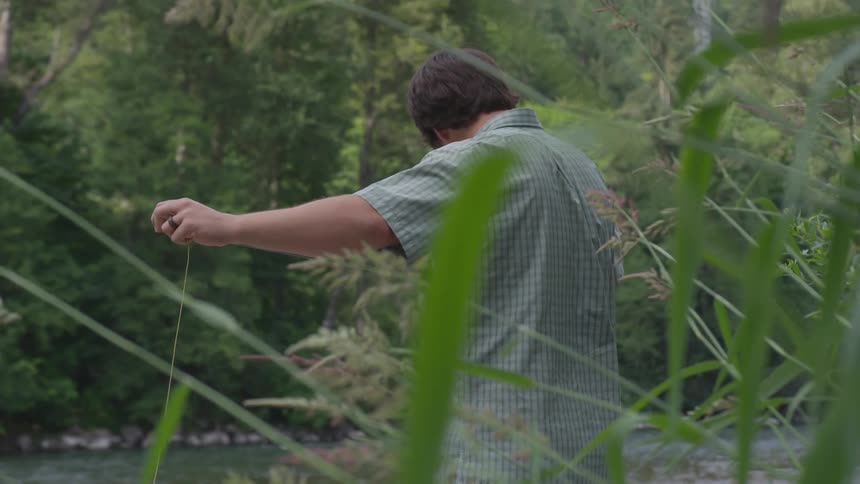 A man standing on the edge of a river measuring out some fishing line