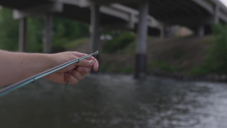 A man near a stream grabs the fishing line that is attached to the fishing pole