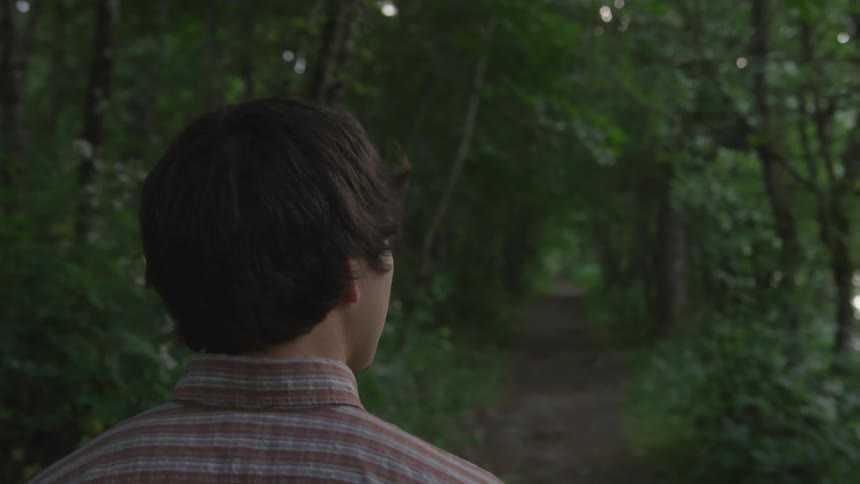A young man walks on a dirt path through the forest