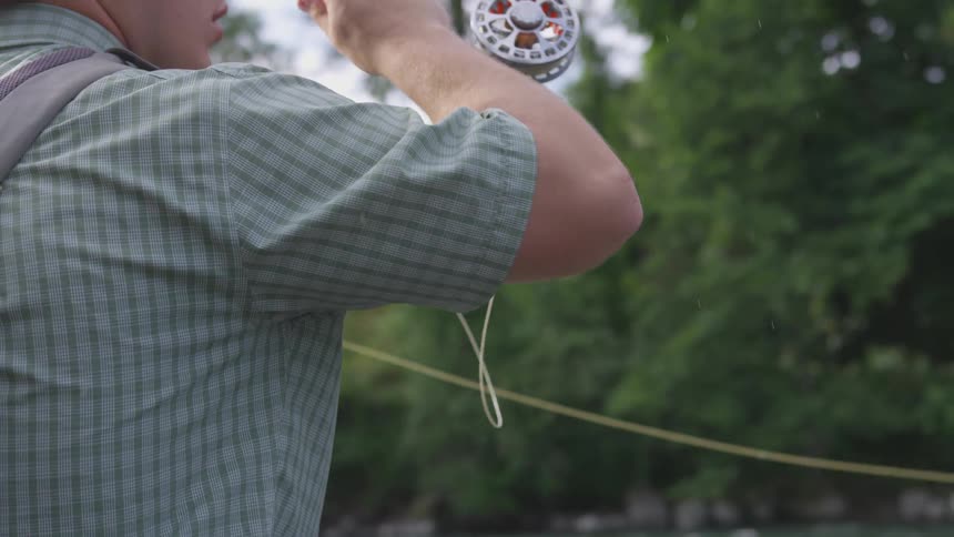 Young man in plaid shirt casting his fly fishing line into a river