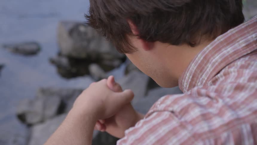 Man wearing red striped shirt clasps hands by the seaside at dusk