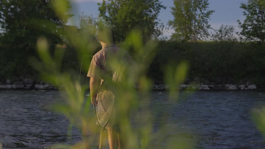 A young man fly fishing on a river on a sunny day