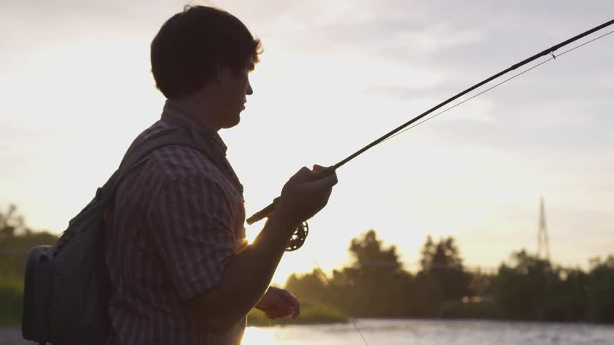 A man is holding a fishing pole at sunset