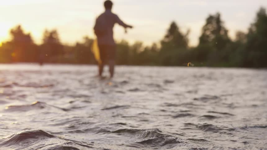 Man standing in moving water fishing at dusk