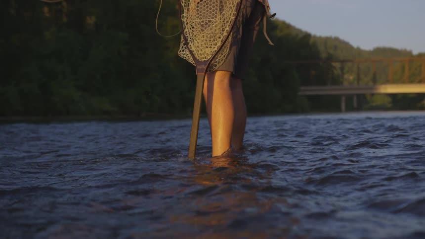 Legs of man standing in water hold a net