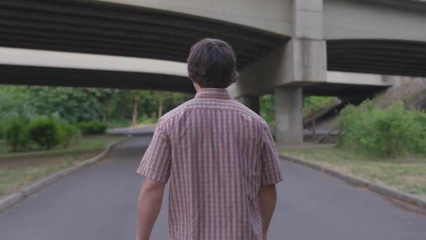 A man in a short sleeve shirt is walking along a paved path that passes under a concrete overpass
