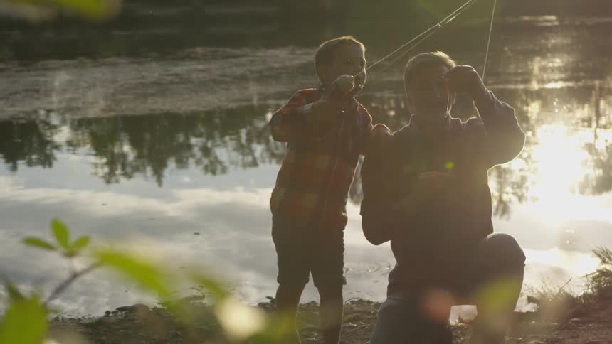An order man helps to hook a worm on the the fishing line of a young boy as they are at the bank of a lake