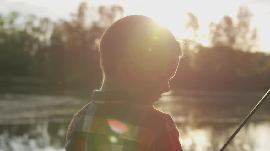 Boy sits near a water with a fishing rod