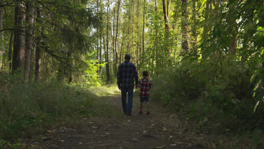 Father and son walking on a trail through the woodsy green forest