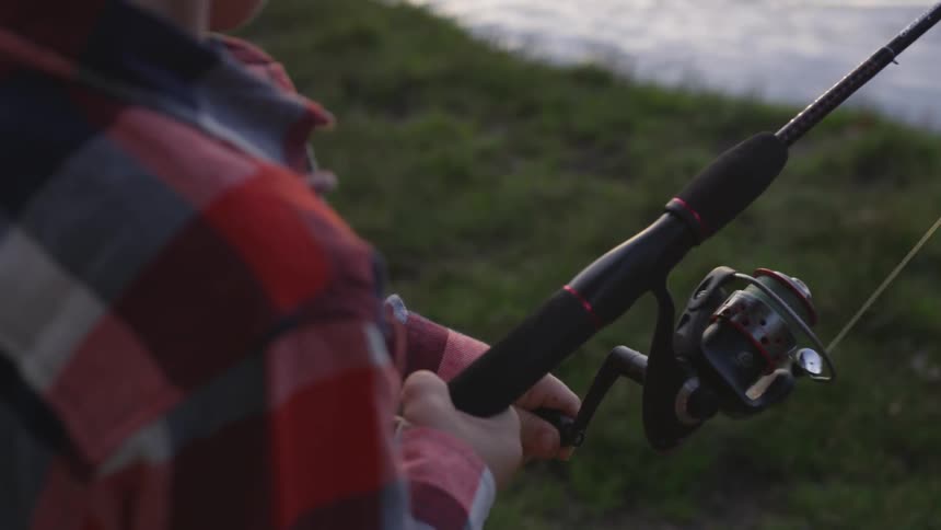 Man reels in fishing line near water during the day